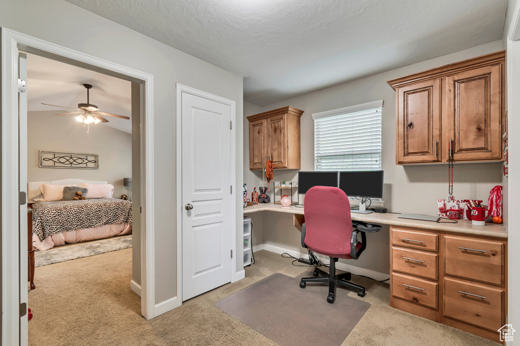 Home office with built in study area, a ceiling fan, baseboards, and light colored carpet