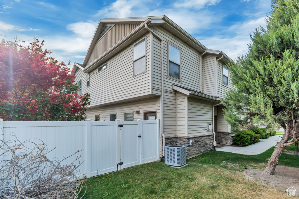 View of side of home featuring a lawn, central AC unit, a gate, fence, and stone siding