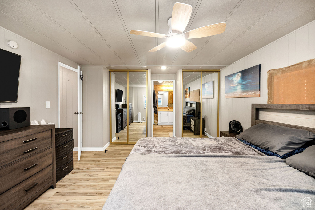 Bedroom featuring ensuite bath, light wood-style flooring, two closets, a ceiling fan, and baseboards