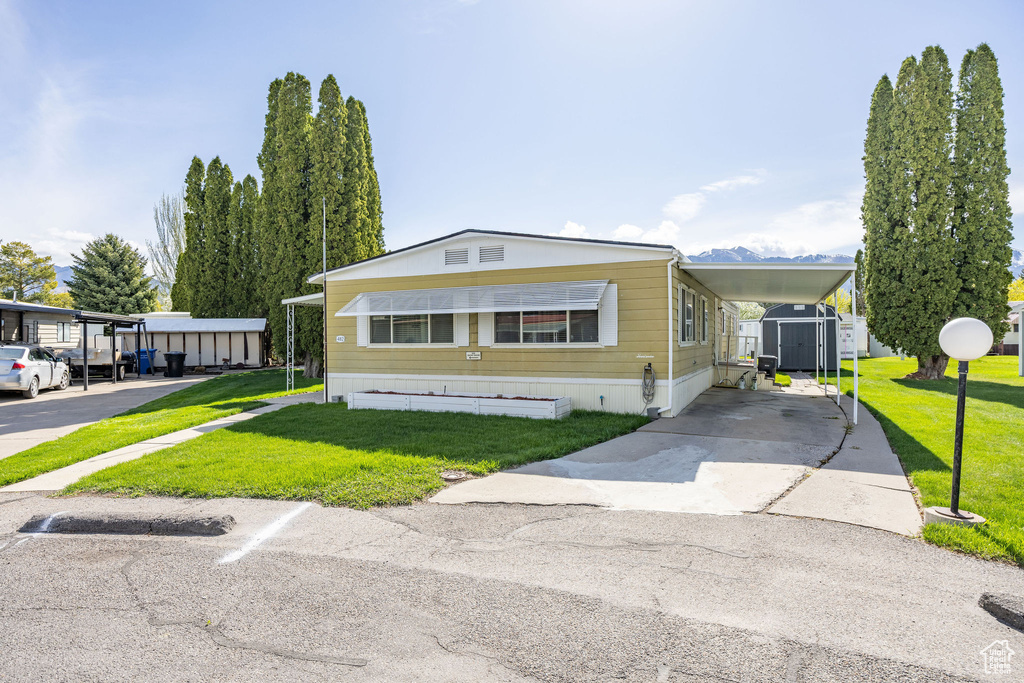 Manufactured / mobile home with an outbuilding, a shed, a front lawn, concrete driveway, and an attached carport
