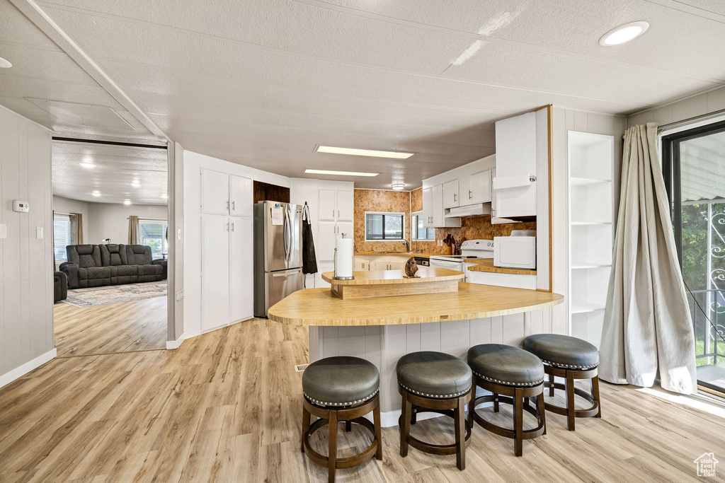 Kitchen with white appliances, a peninsula, under cabinet range hood, and light wood-style flooring