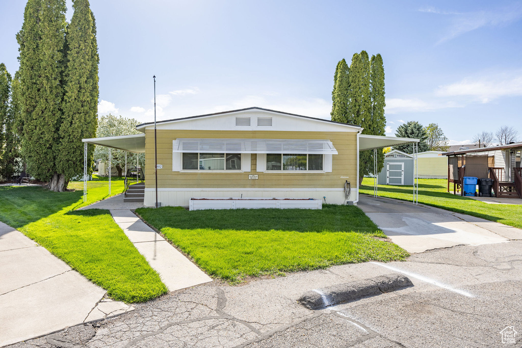 Manufactured / mobile home with a storage unit, an outdoor structure, a front lawn, and a carport