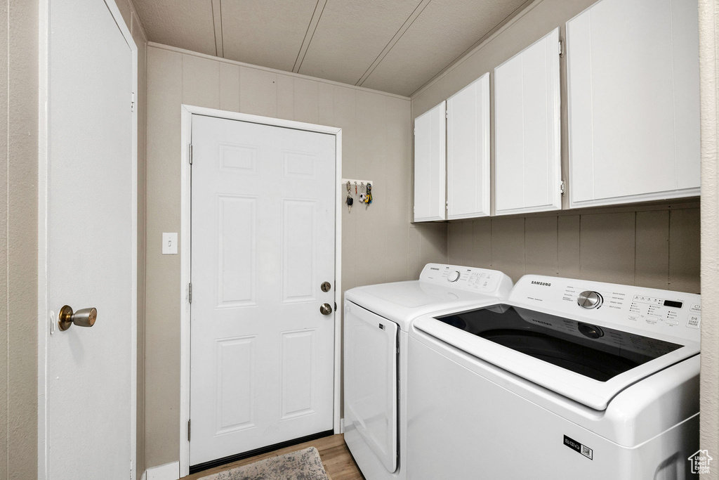 Clothes washing area with light wood-style flooring, cabinet space, and washing machine and dryer
