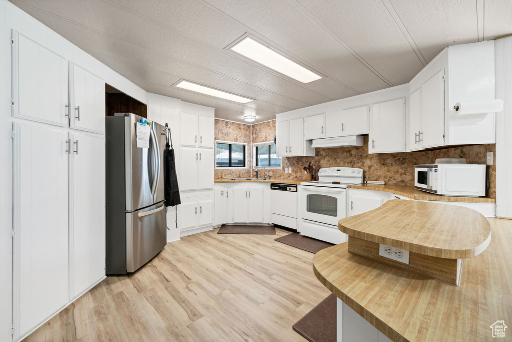 Kitchen featuring white appliances, under cabinet range hood, white cabinets, a sink, and light wood finished floors