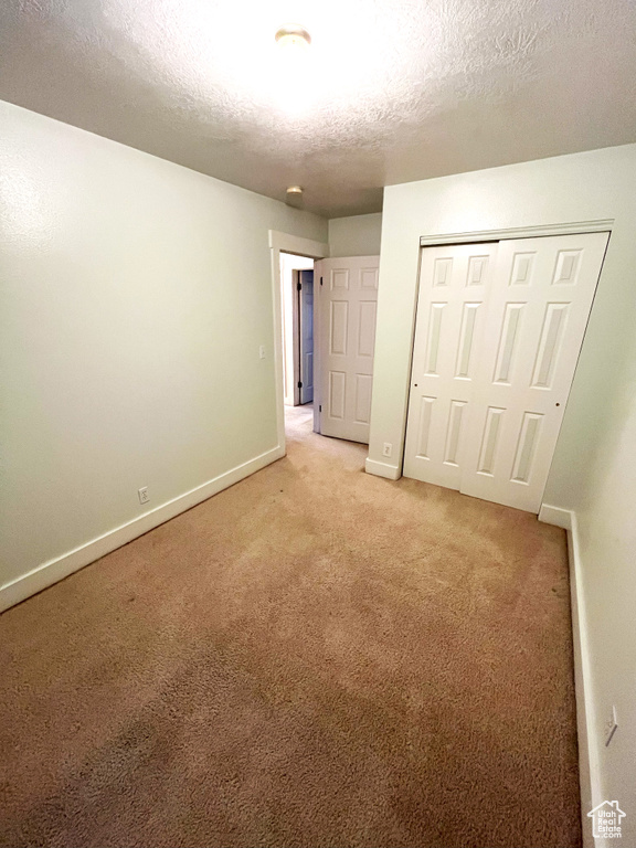 Unfurnished bedroom featuring a textured ceiling, baseboards, and light colored carpet