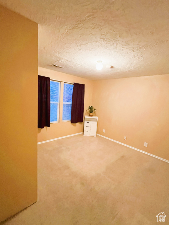 Spare room featuring baseboards, visible vents, a textured ceiling, and light colored carpet