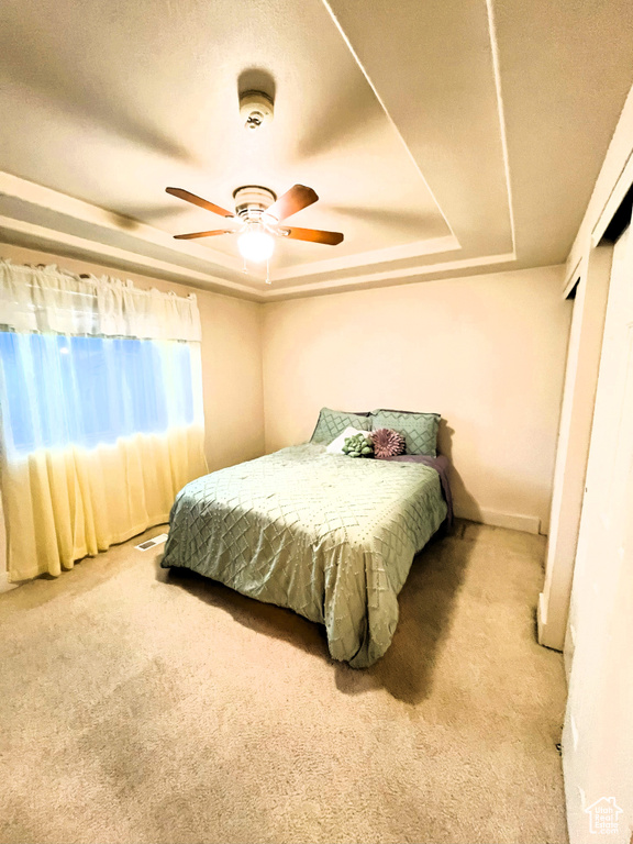 Carpeted bedroom featuring ceiling fan and a tray ceiling