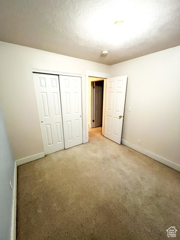 Unfurnished bedroom with a textured ceiling, baseboards, light carpet, and a closet