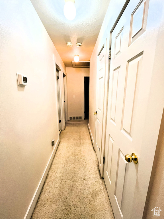 Hall with baseboards, light colored carpet, and visible vents