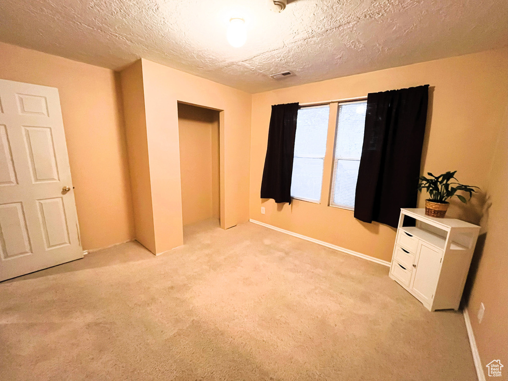Unfurnished bedroom featuring a textured ceiling, visible vents, light carpet, and baseboards