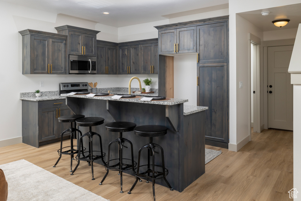 Kitchen featuring appliances with stainless steel finishes, baseboards, a breakfast bar area, and light wood finished floors