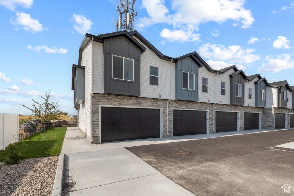 Exterior space featuring fence, a residential view, stone siding, a garage, and board and batten siding