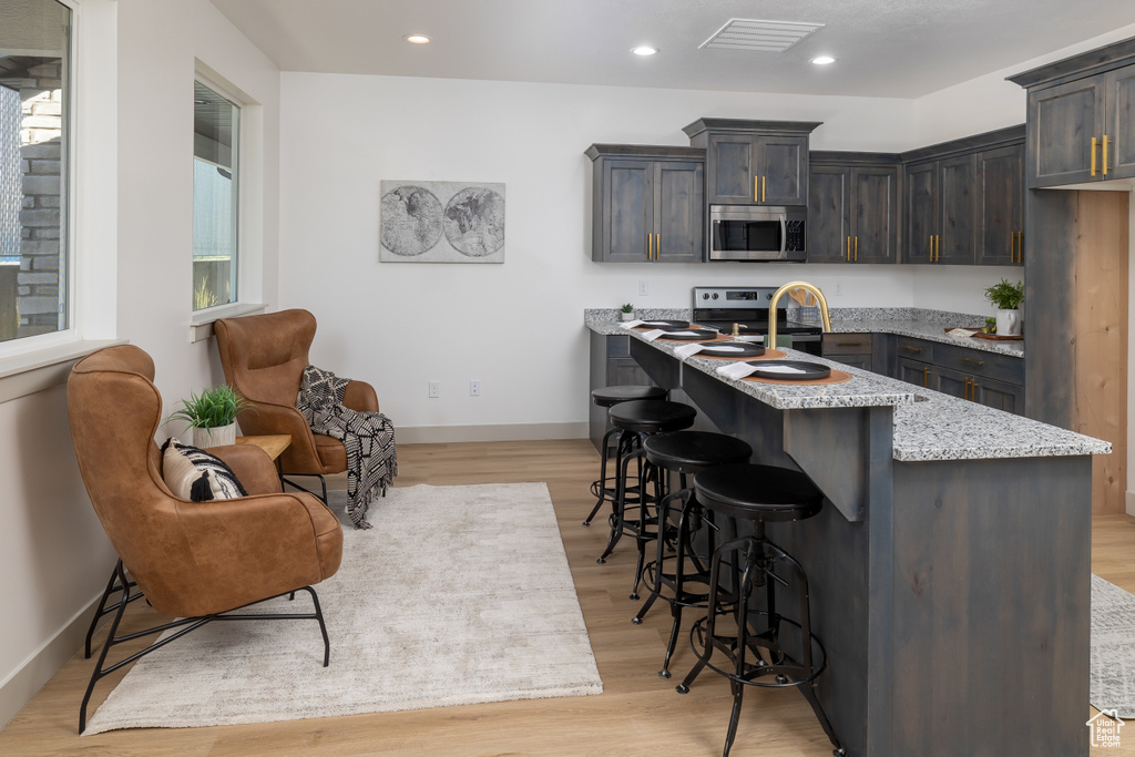 Kitchen with light stone counters, stainless steel appliances, recessed lighting, a kitchen bar, and visible vents