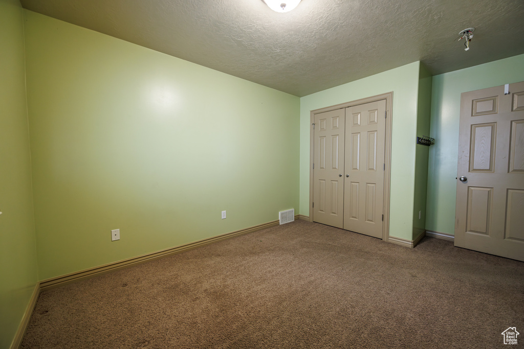 Unfurnished bedroom with visible vents, a closet, baseboards, a textured ceiling, and carpet flooring