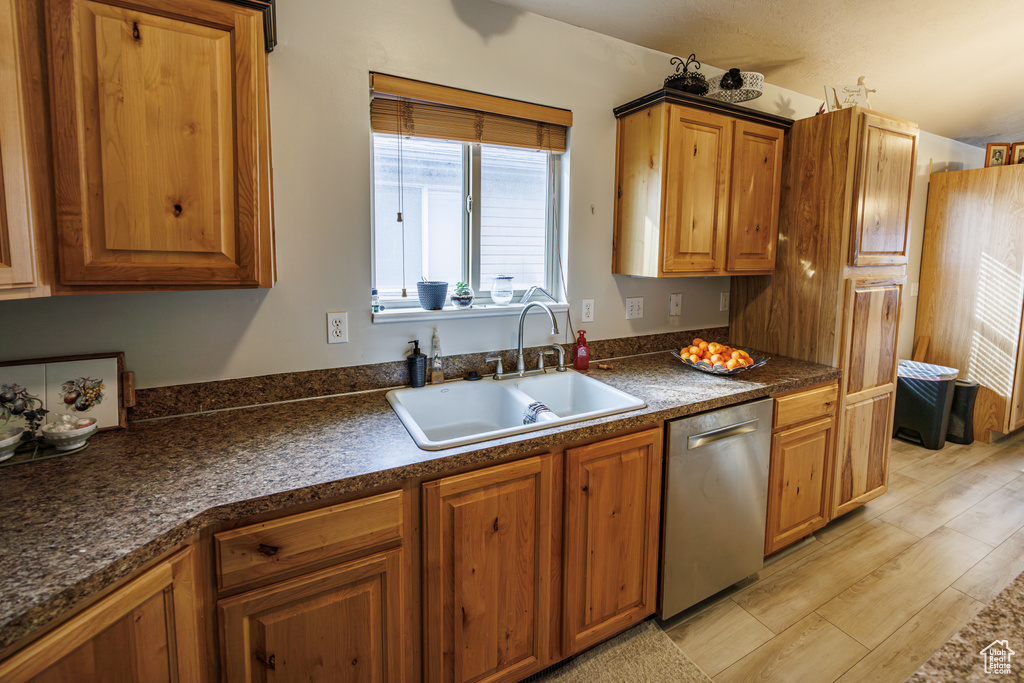 Kitchen with brown cabinetry, dark countertops, dishwasher, a sink, and light wood-style flooring