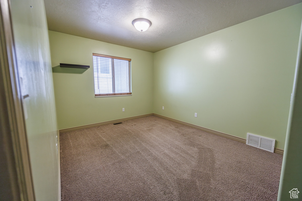 Carpeted spare room featuring a textured ceiling, visible vents, and baseboards