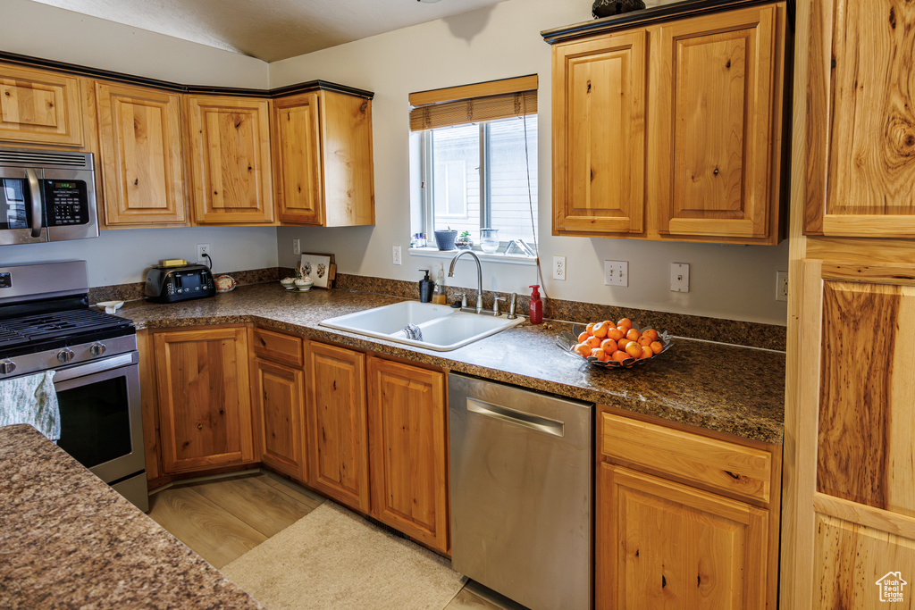 Kitchen featuring a sink, appliances with stainless steel finishes, vaulted ceiling, and dark countertops