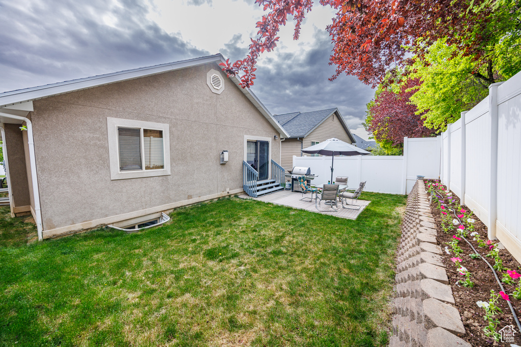 Rear view of property featuring stucco siding, a fenced backyard, entry steps, a lawn, and a patio