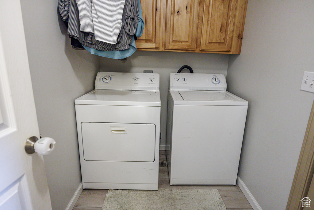 Laundry room featuring cabinet space, baseboards, washer and clothes dryer, and light wood-style flooring