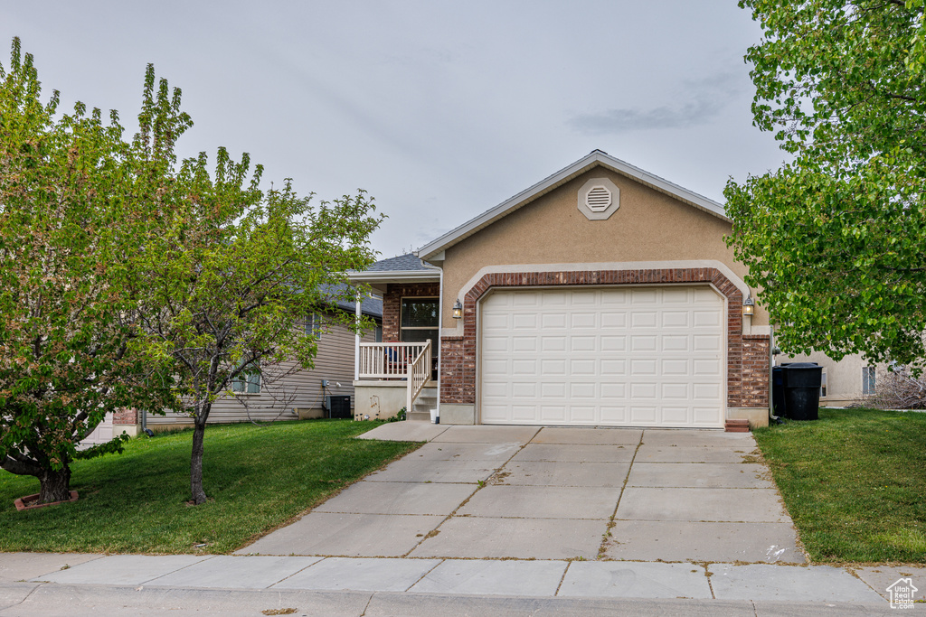 Single story home featuring driveway, a garage, brick siding, a front lawn, and stucco siding