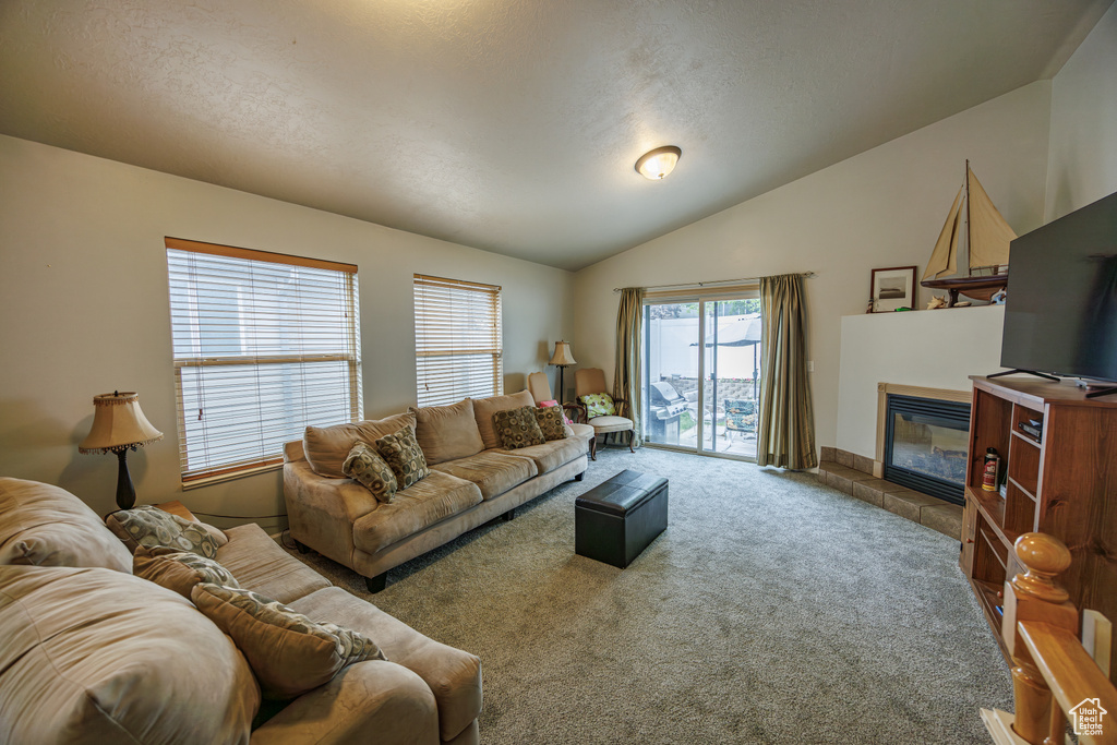 Living area featuring a textured ceiling, lofted ceiling, a tiled fireplace, and carpet