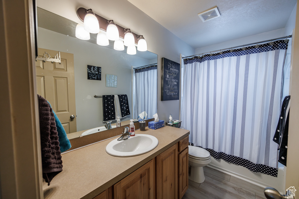 Bathroom with visible vents, wood finished floors, vanity, toilet, and shower / tub combo with curtain