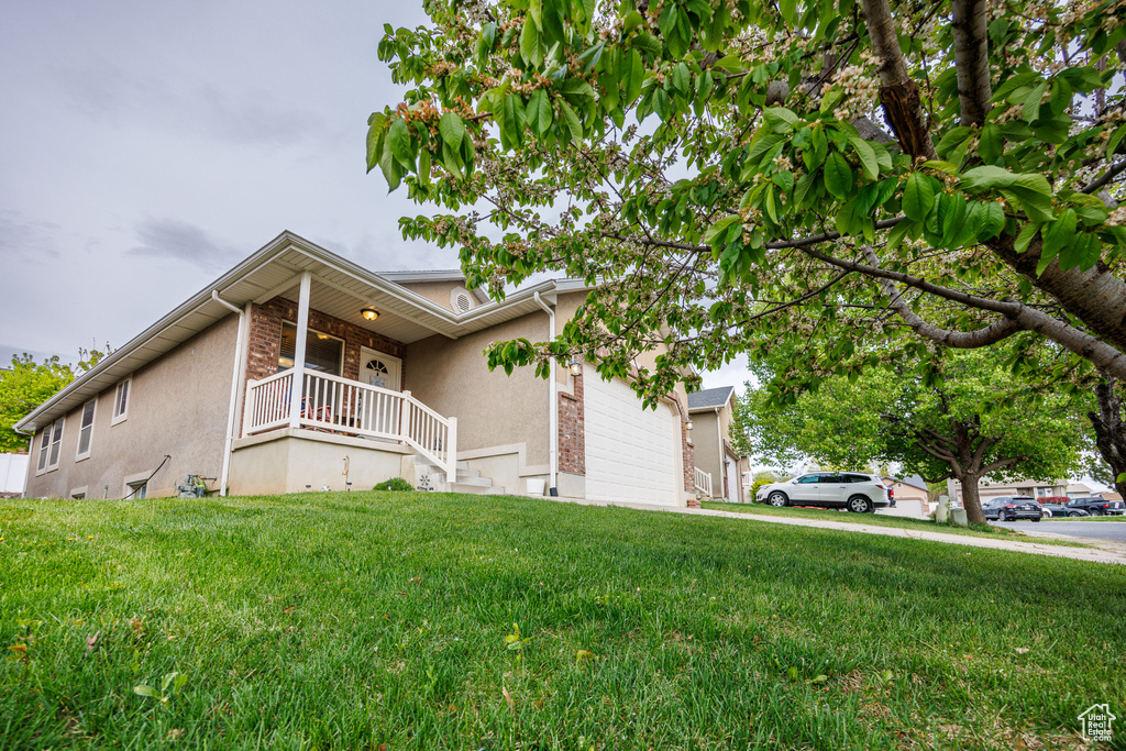 View of side of property with covered porch, a lawn, an attached garage, and stucco siding