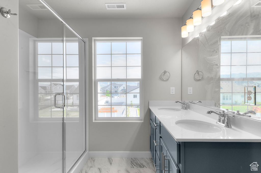 Full bathroom featuring double vanity, marble look tiles, a stall shower, and baseboards