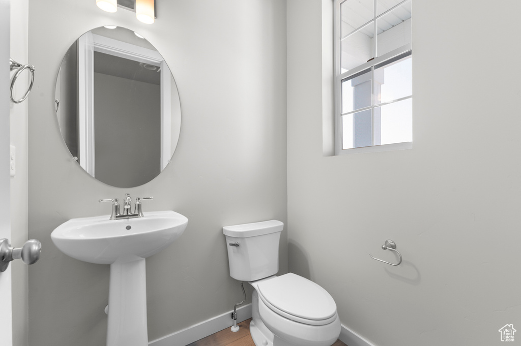 Half bathroom with toilet, baseboards, a sink, and wood finished floors