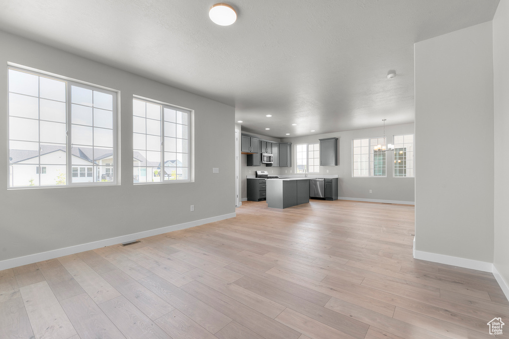 Unfurnished living room featuring a chandelier, baseboards, light wood-style flooring, and recessed lighting