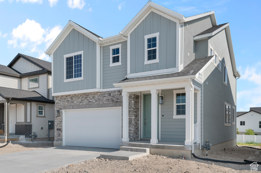 View of front facade with board and batten siding, an attached garage, driveway, stone siding, and covered porch