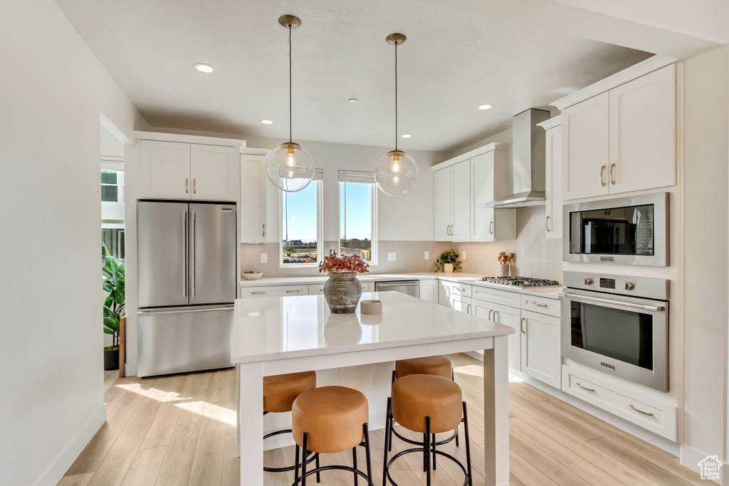 Kitchen with appliances with stainless steel finishes, a kitchen island, light wood-type flooring, and wall chimney exhaust hood