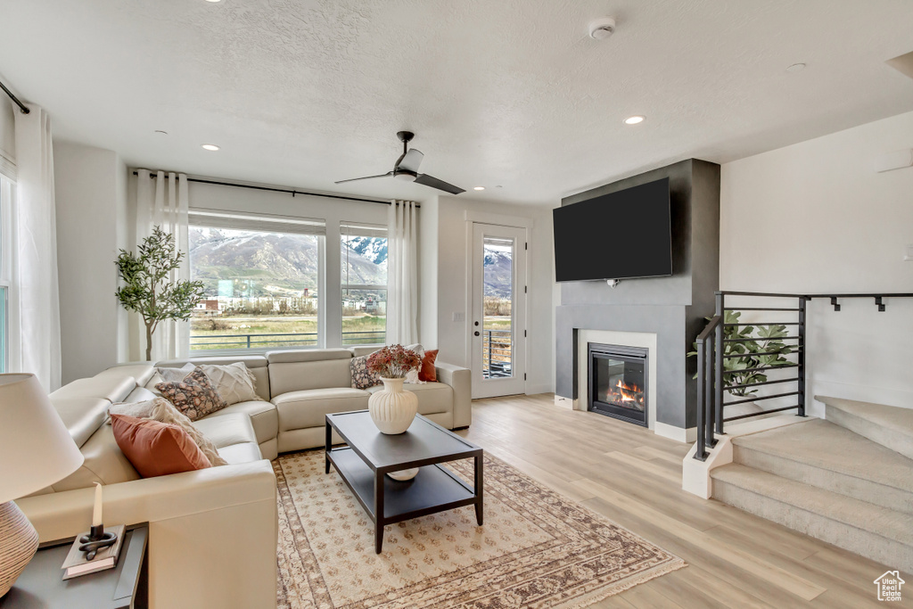 Living area with stairs, a glass covered fireplace, baseboards, light wood-type flooring, and recessed lighting
