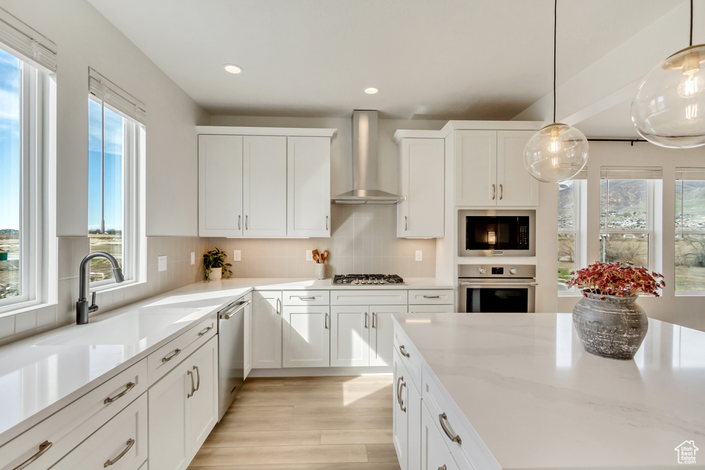 Kitchen featuring light wood-style flooring, appliances with stainless steel finishes, a wealth of natural light, and wall chimney range hood