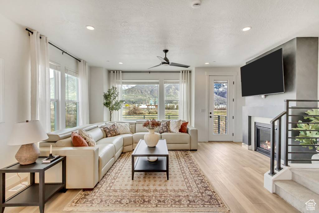 Living room featuring a glass covered fireplace, baseboards, recessed lighting, a ceiling fan, and light wood-style flooring