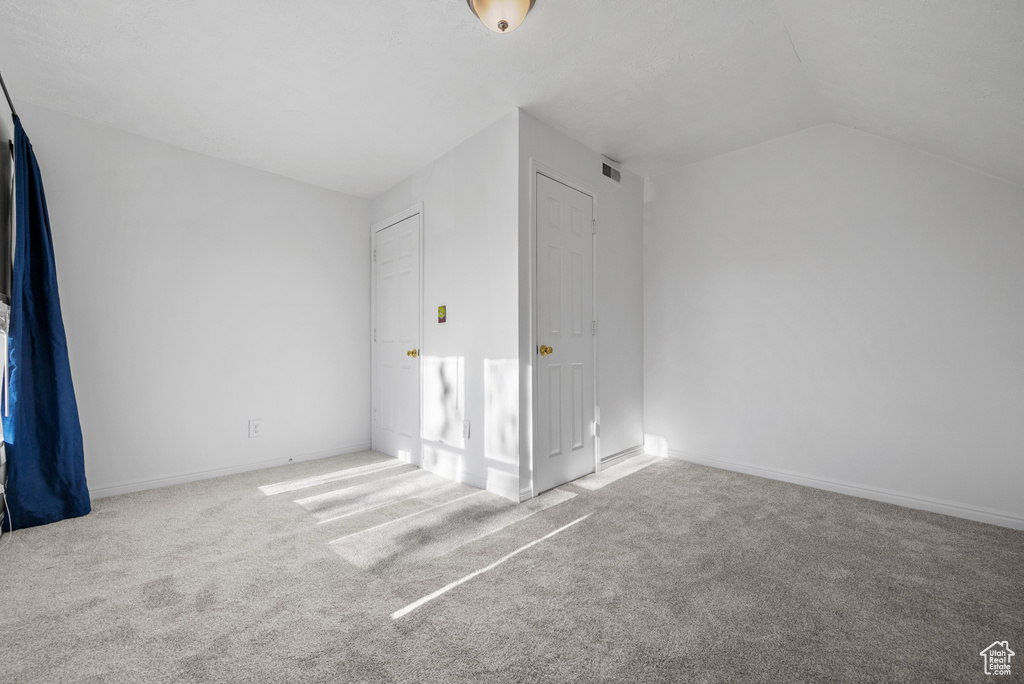 Unfurnished bedroom featuring vaulted ceiling, visible vents, baseboards, and carpet