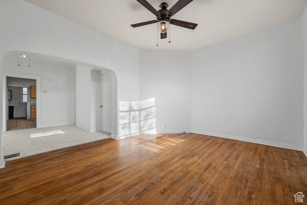 Empty room featuring visible vents, baseboards, arched walkways, hardwood / wood-style flooring, and a ceiling fan