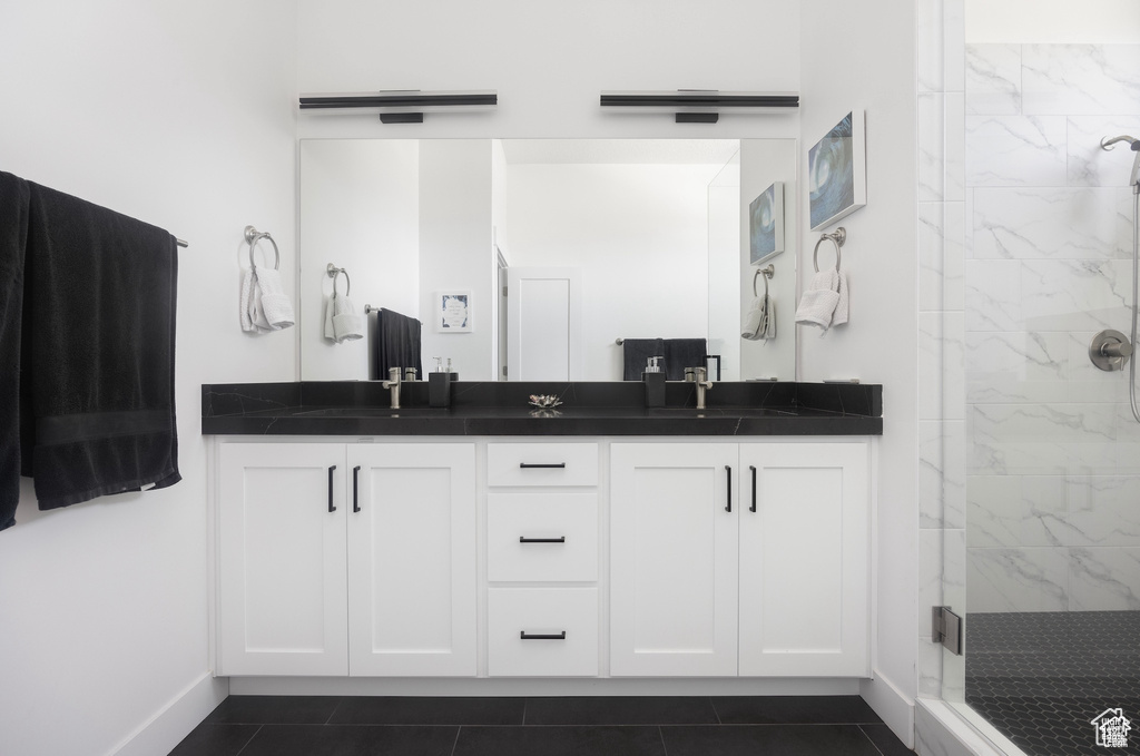 Full bath featuring double vanity, a marble finish shower, and tile patterned floors