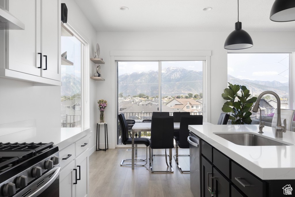Kitchen with light wood-type flooring, a sink, light countertops, under cabinet range hood, and a wealth of natural light