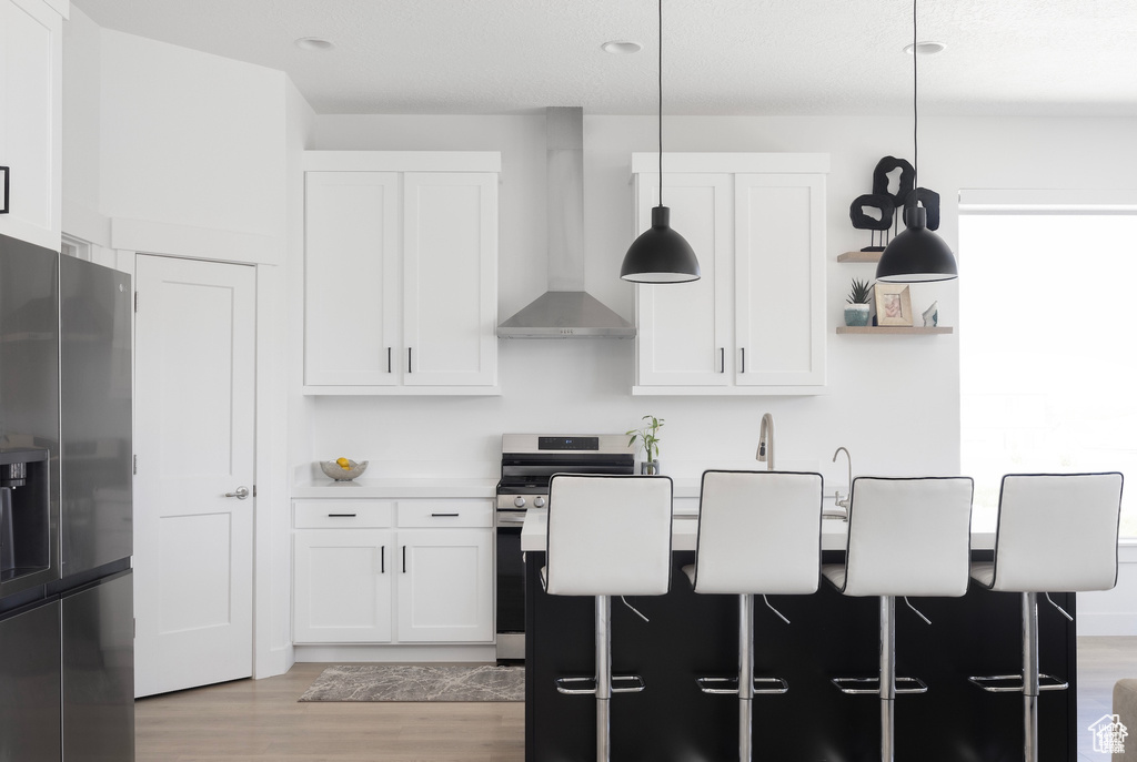 Kitchen with wall chimney range hood, white cabinets, stainless steel appliances, and light wood-type flooring