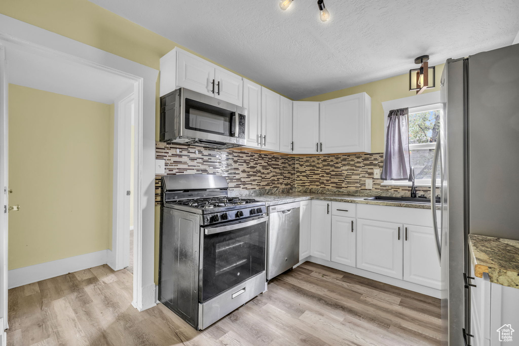 Kitchen featuring white cabinets, appliances with stainless steel finishes, a sink, light wood finished floors, and tasteful backsplash