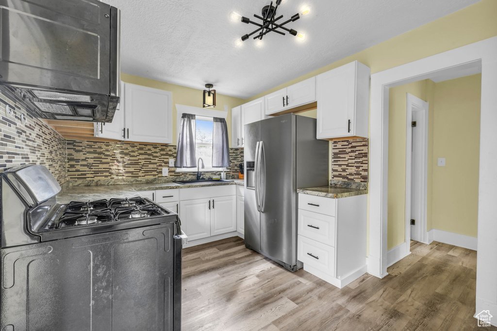 Kitchen featuring white cabinets, stainless steel fridge with ice dispenser, a sink, backsplash, and range with gas cooktop