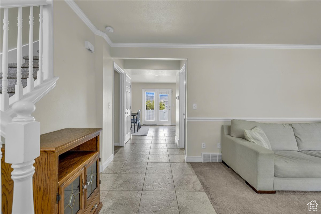 Living room with crown molding, baseboards, stone tile flooring, and visible vents