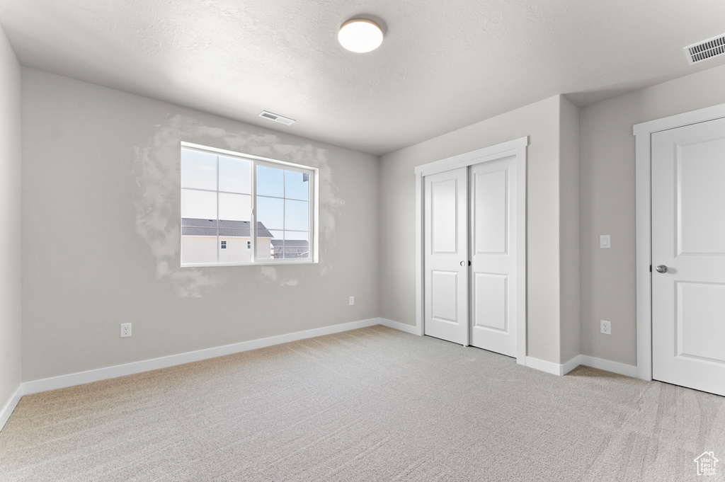 Unfurnished bedroom with light colored carpet, baseboards, and a closet
