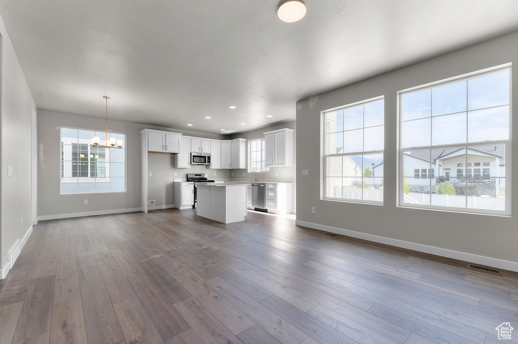 Unfurnished living room with a chandelier, baseboards, plenty of natural light, and recessed lighting