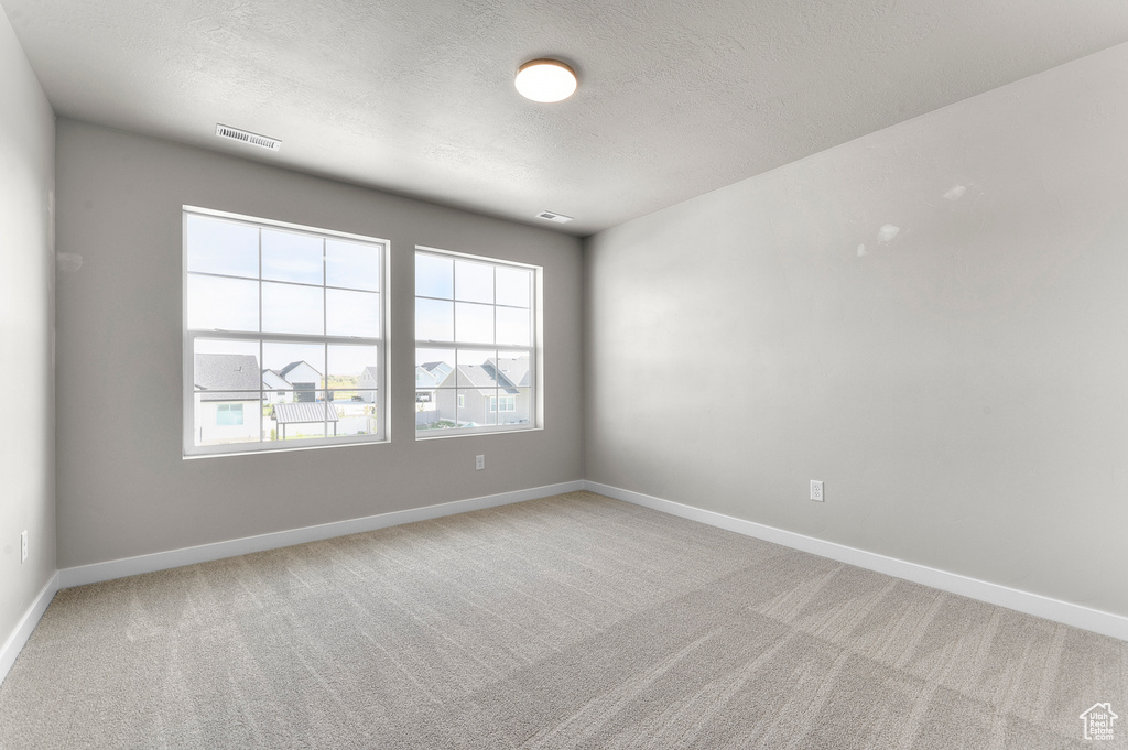 Spare room featuring a textured ceiling, light carpet, and baseboards