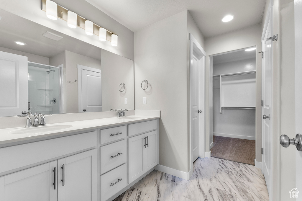 Full bath with double vanity, a stall shower, marble finish flooring, a spacious closet, and baseboards