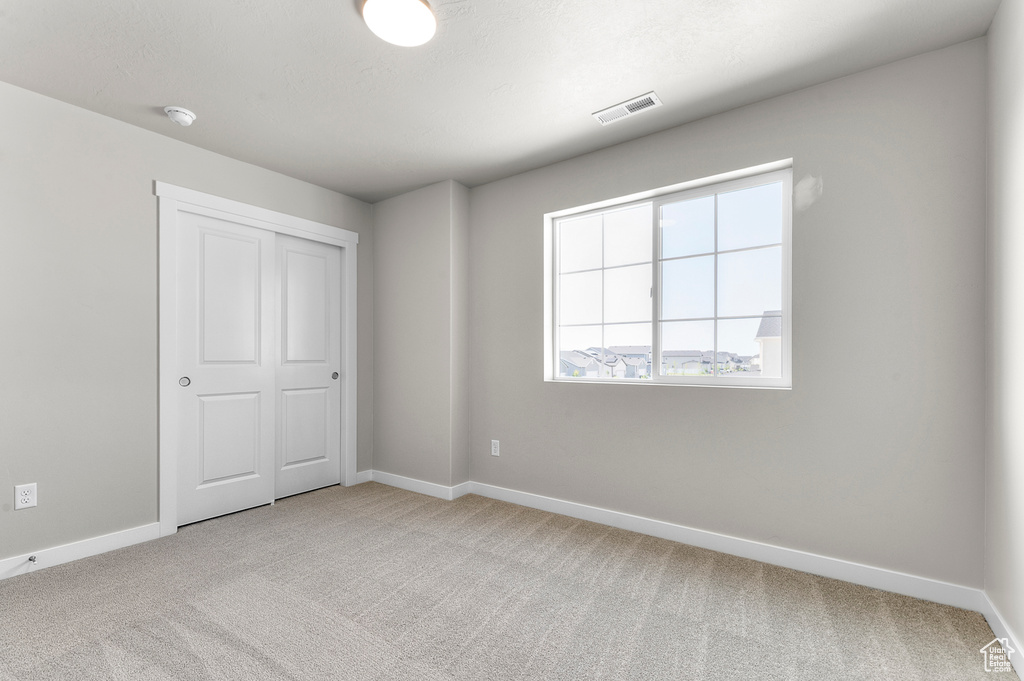 Unfurnished bedroom with light carpet, baseboards, and a closet