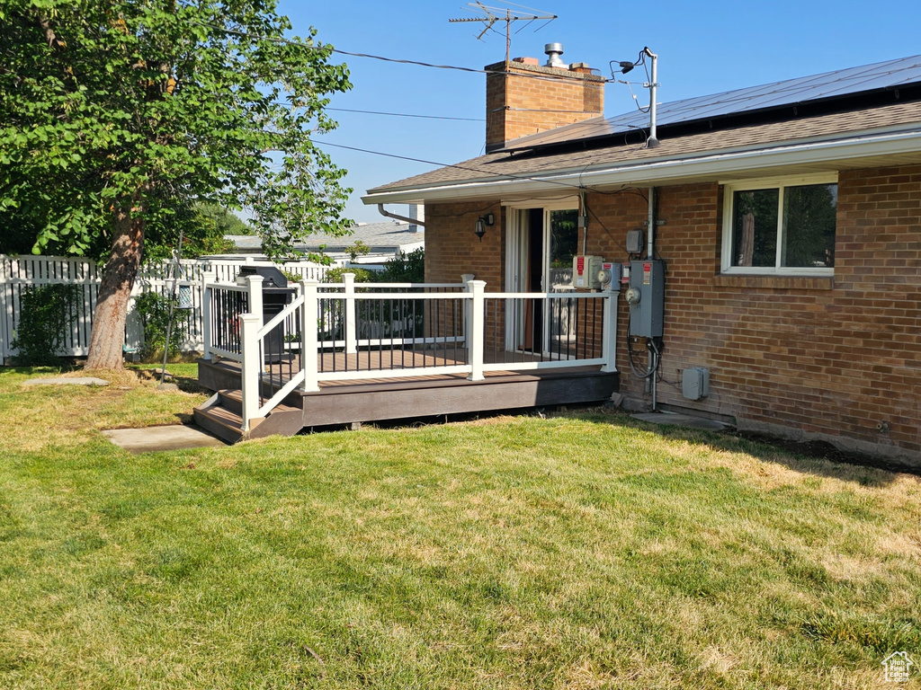 Rear view of house featuring a chimney, brick siding, a wooden deck, roof mounted solar panels, and a shingled roof
