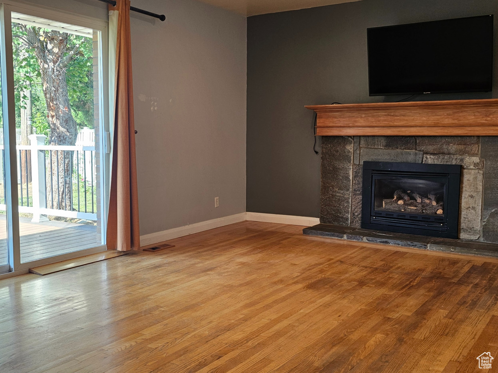 Unfurnished living room with healthy amount of natural light, wood finished floors, and a stone fireplace